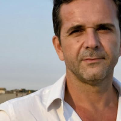 Marco Célio Sousa, de camisa blanca, en la playa al atardecer.